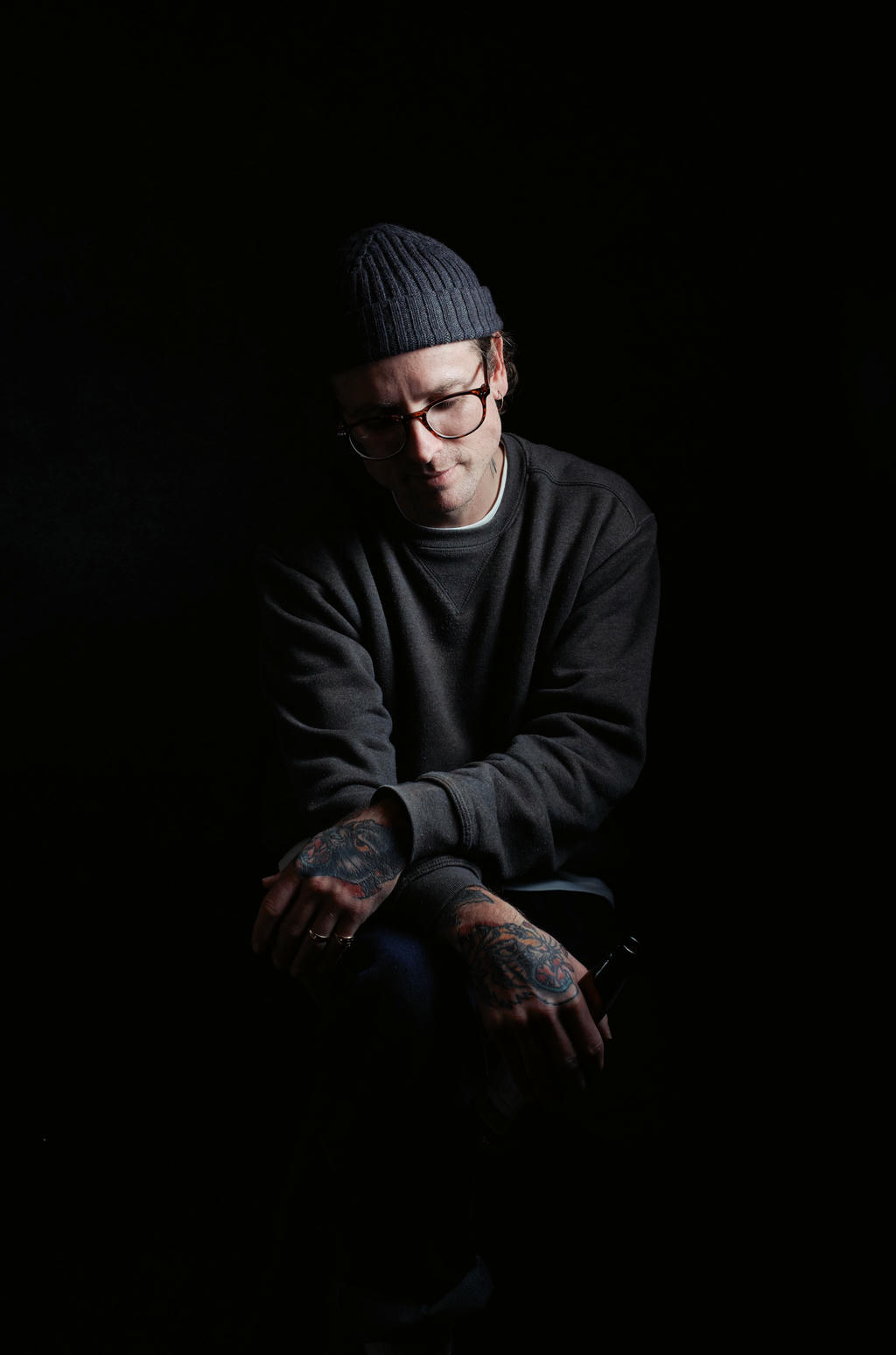 A man looking down to the ground whilst holding a beer in tattooed hands