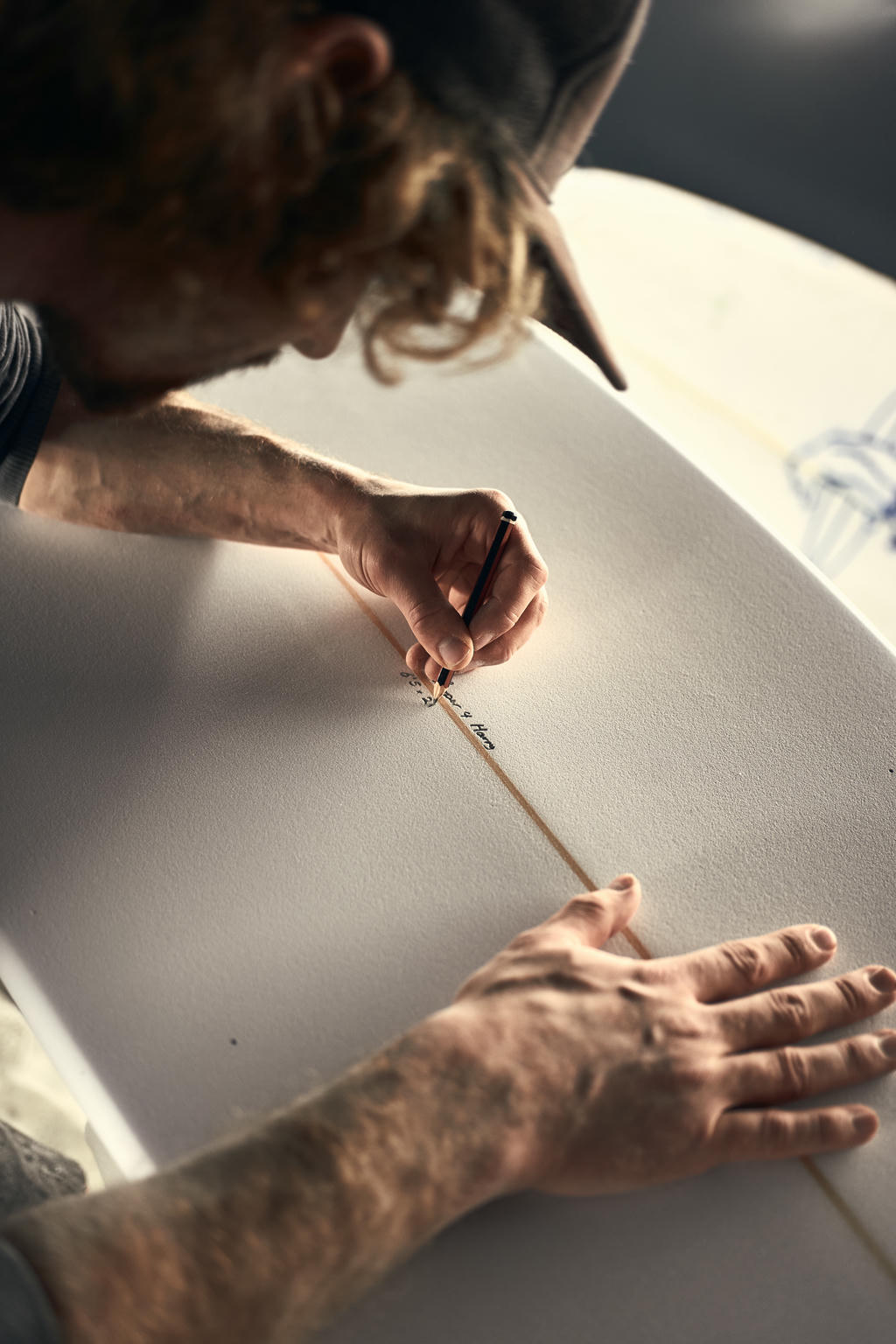 Ollie Cooper adding the dimensions to a surfboard with a pencil